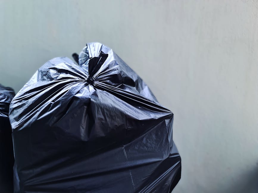 A large green wheelie bin filled with bags of gardening or building materials, including several red and black bags labeled 'FLEXLEADER CZE S1' and 'FK200 FLEXY PLUS', is positioned on a paved area ag