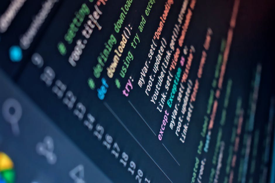 A close-up photograph of a computer screen displaying lines of colorful programming code in various shades of red, green, blue, and yellow against a dark background. The code contains syntax elements 